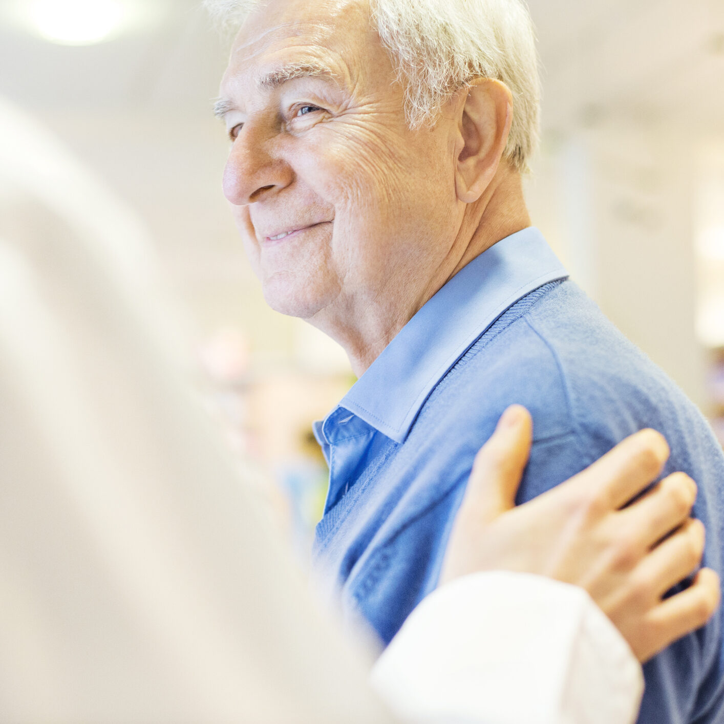 Cropped image of female pharmacist consoling senior man in store. Smiling male customer is looking at chemist. They are at brightly lit pharmacy.